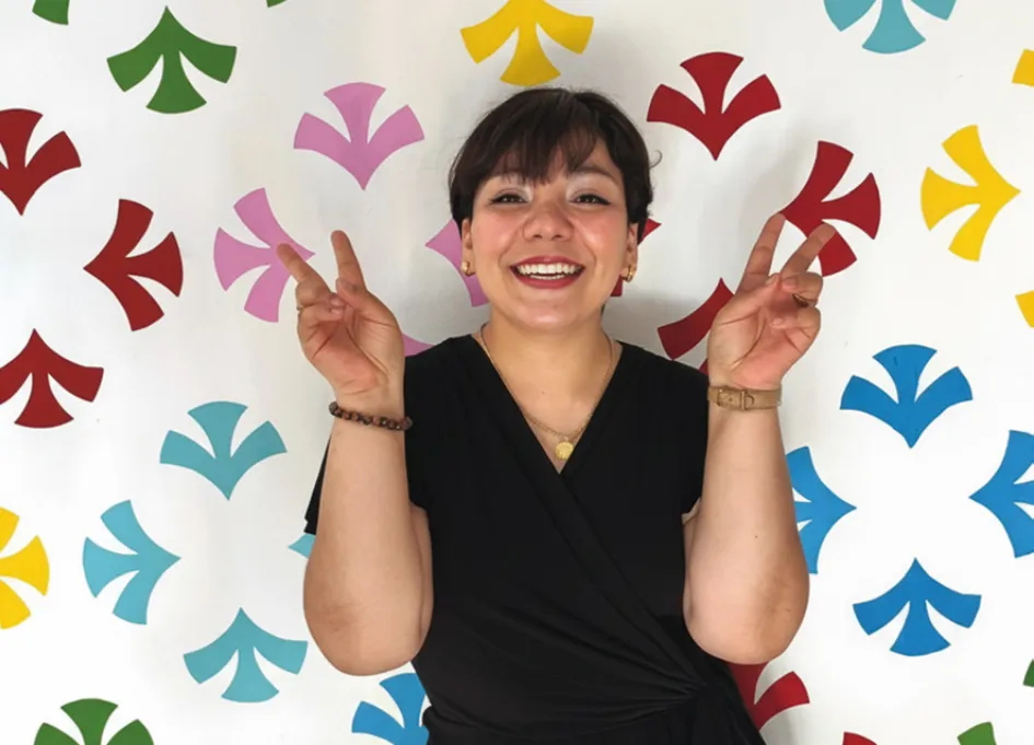 Mafe Guerrero sonriente frente a un muro con patrón gráfico de colores